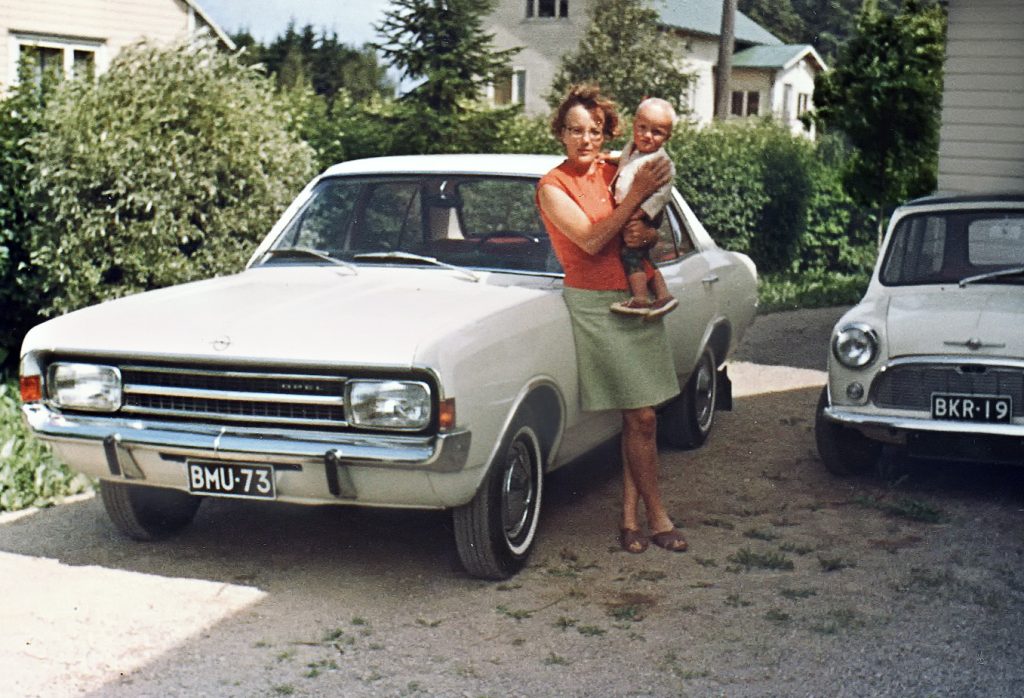 1960-luvun valokuva, jossa nainen nojaa autoon laps sylissään